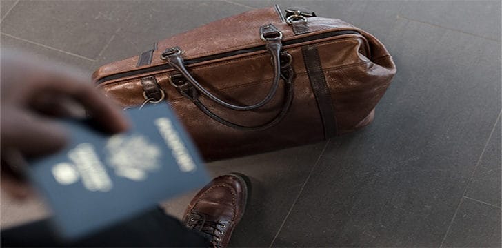 passaporto e borsa Persona che regge un passaporto con valigia sullo sfondo.